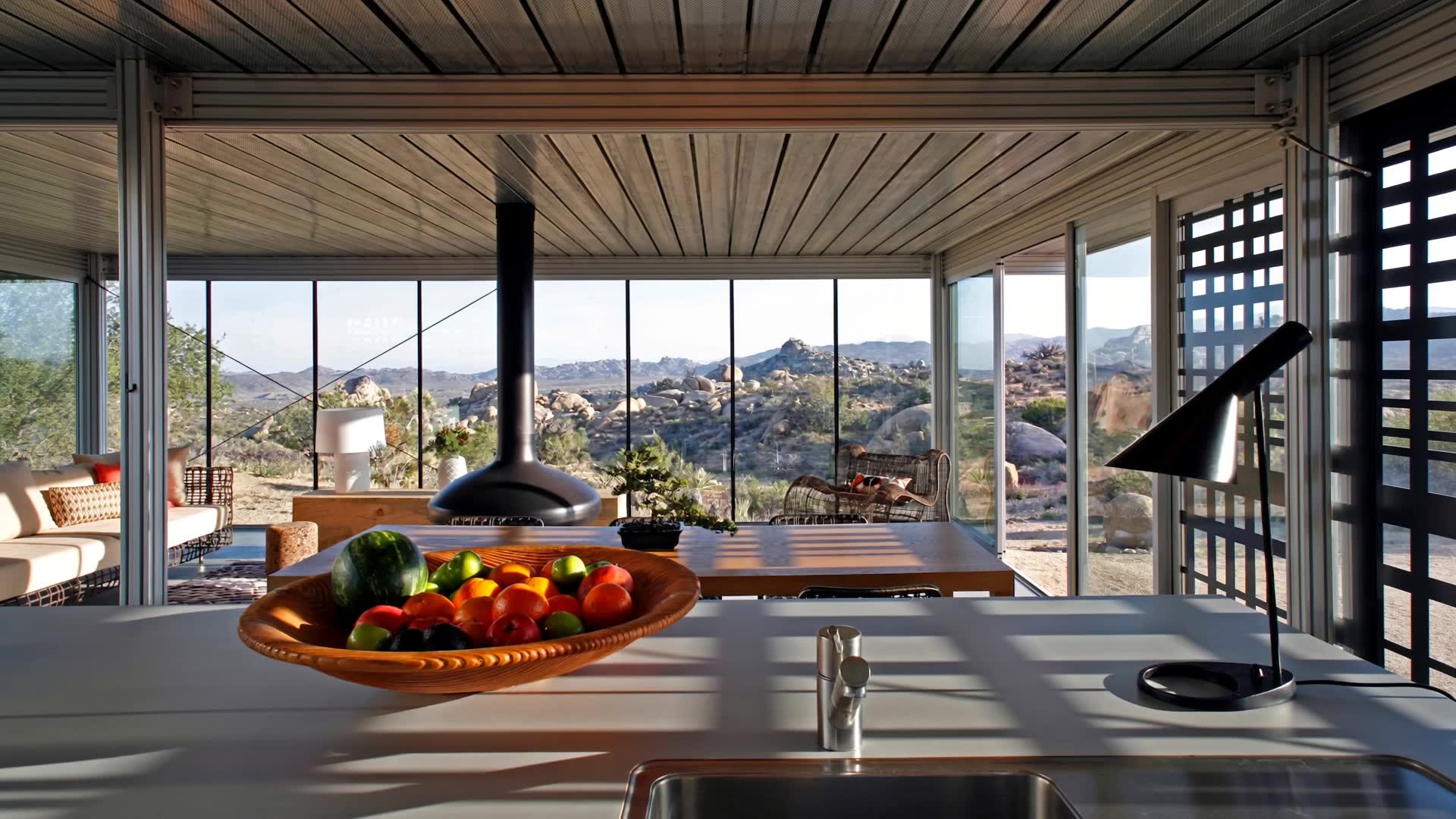 Video walk-through of a glass-walled desert home, from the kitchen to a bedroom with boulder views