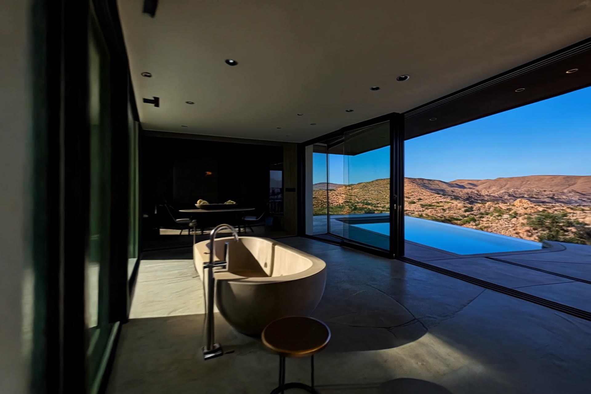 Sunlit desert retreat with a stone bathtub and glass walls opening onto an infinity pool